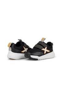 Zapatillas de malla negra con suela blanca, acentos en naranja y gris, con correas de Velcro y un acabado texturizado.