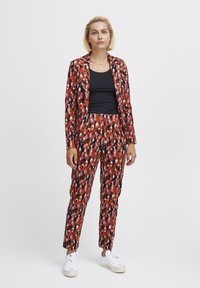 Piros és fekete mintás öltöny, szabott zakóval és slim-fit nadrágokkal, fekete toppal és fehér sportcipőkkel párosítva.
