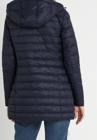 Tmavě námořnická polstrovaná bunda s kapucí, s vodorovnými prošívanými linkami a mírně prodlouženým střihem. Vyrobena z hladké látky.