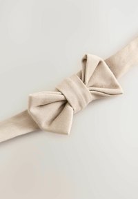 Beige kangasvyö, jossa suuri rusetti keskellä. Materiaali on teksturoitu ja tuntuu pehmeältä ja sileältä.