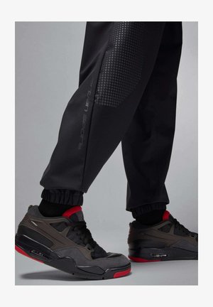 Sneaker da atletica grigie con accenti rossi, caratterizzate da una parte superiore testurizzata e da un'ammortizzazione ad aria. Abbinate a pantaloni jogger neri a gamba stretta con polsini elastici.