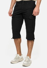 Shorts cargo noirs avec un design jusqu'au genou, plusieurs poches et ourlets ajustables à cordon. Fabriqués en tissu durable avec des coutures visibles.