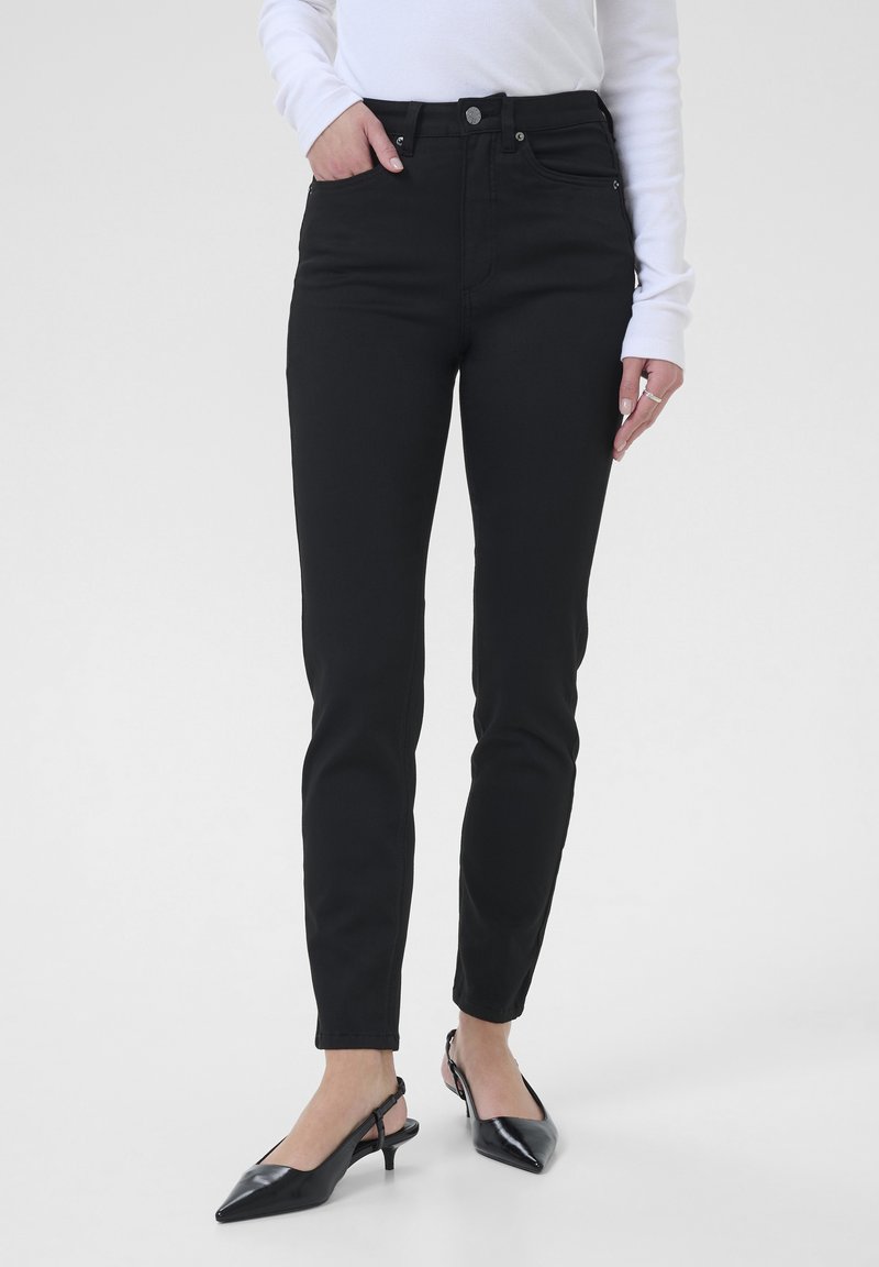 Jean taille haute noir avec une coupe slim. Tissu en mélange de coton, poches avant et fermeture à bouton. Associé à des escarpins noirs à talon slingback.