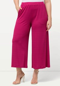 Pantaloni a gamba larga magenta con texture a coste, dotati di una comoda vita elasticizzata e tasche laterali. Abbinati a tacchi con cinturino alla caviglia trasparente.