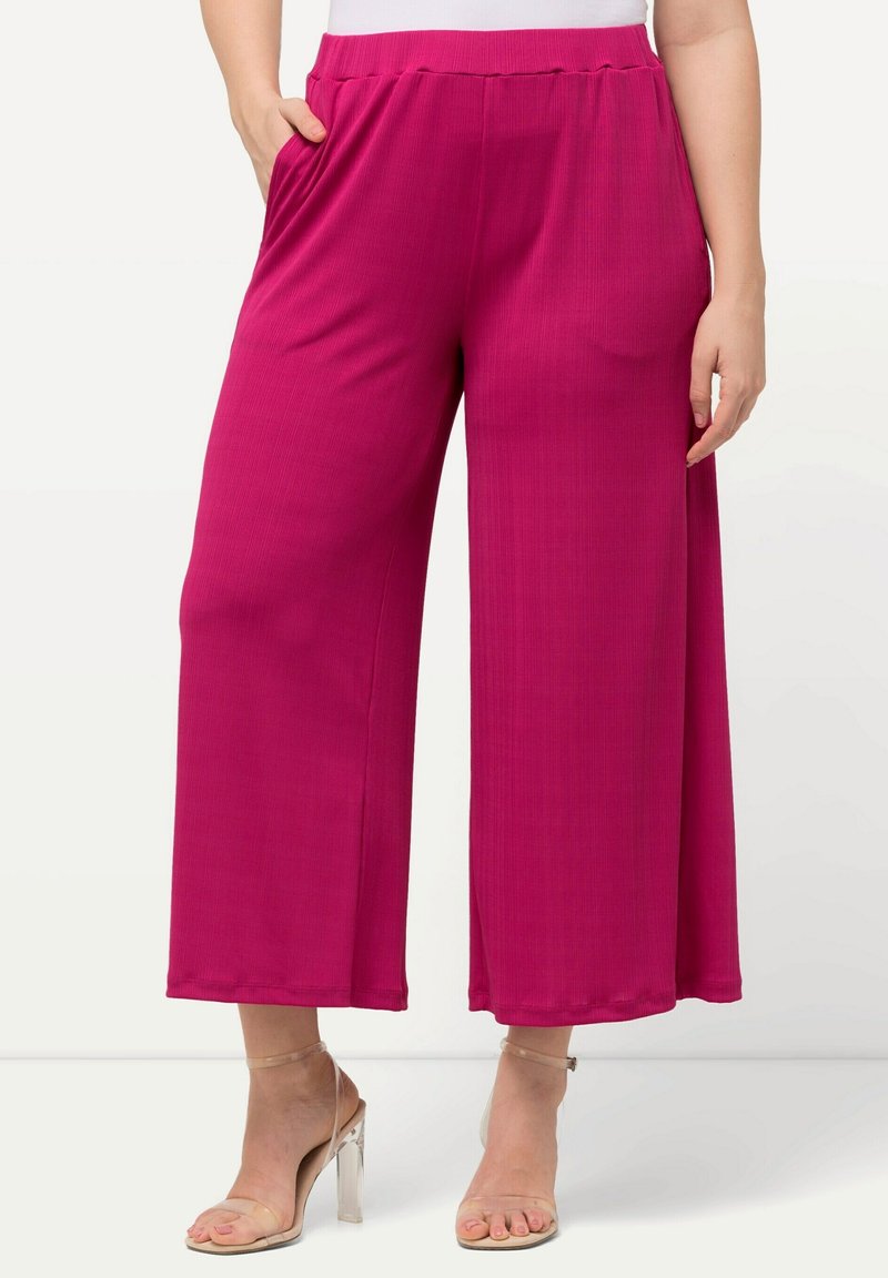 Pantaloni a gamba larga magenta con texture a coste, dotati di una comoda vita elasticizzata e tasche laterali. Abbinati a tacchi con cinturino alla caviglia trasparente.