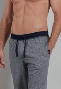 Men's patterned lounge pants in blue and white, featuring an elastic waistband with drawstring, smooth texture, and geometric design.