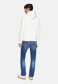 Weißer Kapuzenpullover mit Kängurutasche, kombiniert mit blauen Jeans und weißen Sneakers, von hinten betrachtet, zeigt einen lässigen Look.