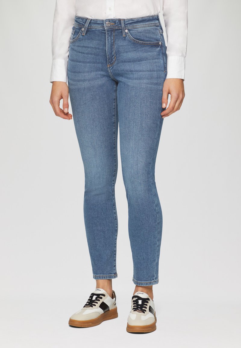 Lichtblauwe skinny jeans van denim, met een vijf-pocket ontwerp, subtiele beschadigingen en een mid-rise taille, gecombineerd met witte sneakers.