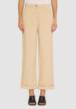 Pantaloni beige ampi e corti con orli risvoltati, bottone frontale e pieghe, indossati con sandali mule neri intrecciati con punta aperta.