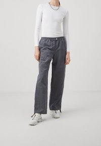 Pantaloni di tessuto leggeri e grigi con una vestibilità rilassata, una cintura elastica e due tasche laterali. Abbinati a un top bianco a maniche lunghe.