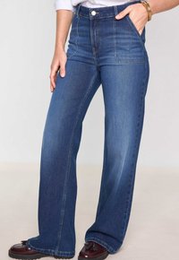 Jeans in denim blu a vita alta con gambe larghe, dotati di tasche anteriori, chiusura con bottone e zip, e una leggera texture scolorita.