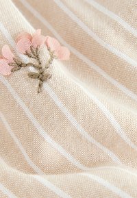 Beiger Stoff mit dünnen weißen Streifen und bestickten rosa Blumen mit grünen Stängeln und Blättern.