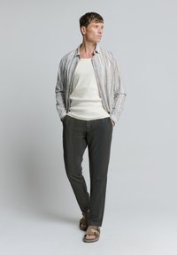 Herenoutfit met een licht gestreepte overhemd met knopen, witte tanktop, donkere broek en bruine sandalen; casual ontwerp met verschillende texturen.