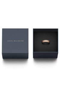 Ruusukultainen sormus tummansinisen laatikon sisällä, jossa on kultainen logo. Sisustus on musta ja pehmeä tekstuuri, joka pitää sormuksen turvallisesti paikoillaan.