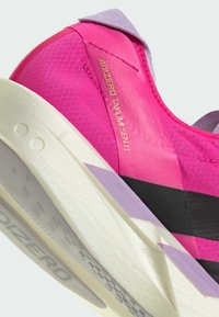 Adizero Takumi Sen 11 tenisice s gornjim dijelom u jarko ružičastoj boji, teksturiranim preklopom, ljubičastim naglascima i bijelim međupotplatom s uzorkom za prianjanje.