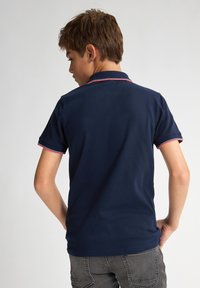 Tmavě modrá polo tričko s límečkem a krátkými rukávy, s červenými akcenty na límci a lemech rukávů. Hladká bavlněná textura.