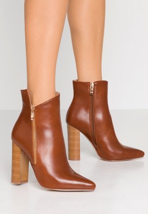 Bottines en cuir marron avec un bout pointu et une fermeture éclair en argent, dotées d'un talon en bloc transparent avec des rayures horizontales.