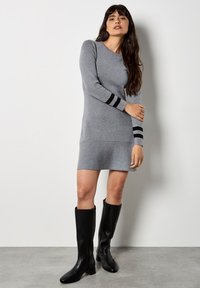 Graues Strickkleid mit langen Ärmeln, das schwarze Streifenakzente an den Bündchen aufweist. Das Kleid hat eine figurbetonte Silhouette und eine weiche Textur.