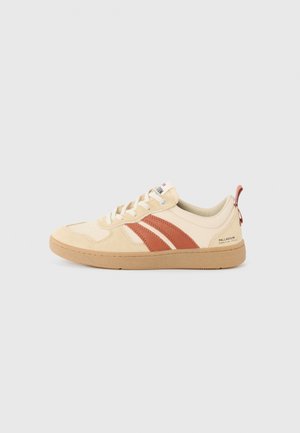Sneaker en suédine beige avec des rayures brunes, un embout texturé et une semelle en caoutchouc beige. Dispose d'une languette et d'un logo au niveau du talon.
