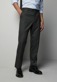 Pantalons de costume gris charbon avec un devant plat, des poches latérales et une coupe slim. Associés à des chaussures en cuir noires et une chemise rayée bleu clair.