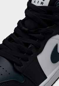 Must ja tumesinine nahast toss, millel on valge külgpaneel, tekstureeritud paelad, täpiline varbalaegas ja türkiissinine Nike Swoosh embleem.