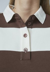 Brun og hvid stribet polo shirt med krave, der har tre brune knapper og et tekstureret stof.