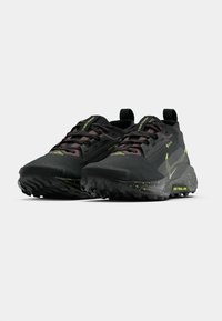 Black trail running shoes with a textured surface, green accents, durable rubber outsoles, and lace-up design with reinforced eyelets.