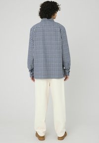 Chemise à carreaux bleus et blancs avec un col, des manches longues et une coupe décontractée, associée à un pantalon crème et des chaussures marron.