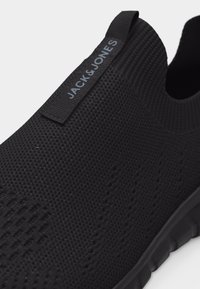 Μαύρο μάλλινο αθλητικό παπούτσι slip-on με υφή και ετικέτα "JACK & JONES" στο πίσω μέρος της φτέρνας.