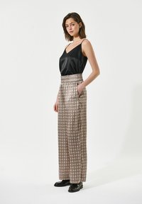 Camisola nera in satin con scollatura a V abbinata a pantaloni larghi crema con motivi geometrici e vita elastica.