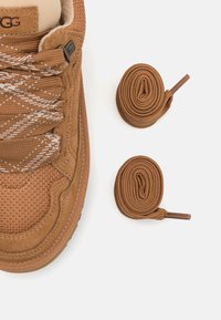 Bruine sneaker van mesh en suede materialen, met een gestructureerde bovenkant, witte gestreepte veters en ronde bruine veters daarnaast.