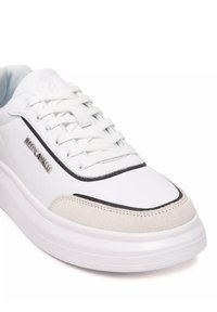 Baskets blanches avec un dessus en cuir lisse, accent en daim gris, bord noir et lacets blancs. Elles disposent d'une semelle extérieure épaisse et solide de couleur blanche.