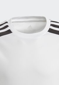 Camisa blanca de manga corta con cuello redondo, que presenta tres franjas negras en cada hombro y una tela suave y ligera.