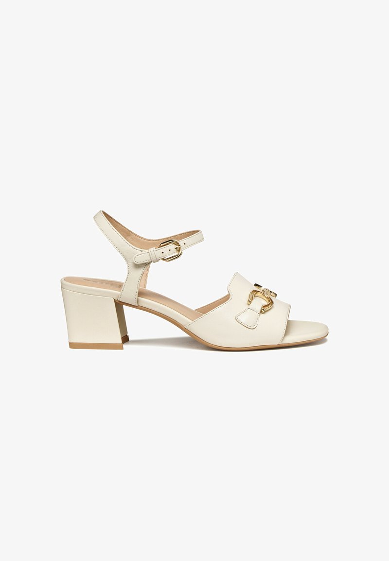 Sandale ouverte en cuir crème, talon bloc, bride de cheville avec bouclier doré, et ornementation dorée sur la bride avant.