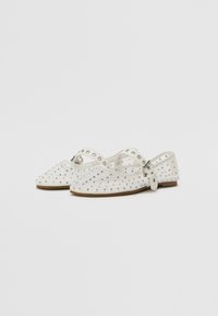 White flat shoes with a rounded toe, studded with silver rhinestones, featuring an adjustable strap and a flat brown sole.