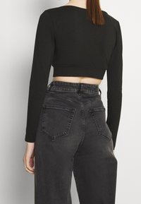 Black cropped long-sleeve top with a round neckline paired with high-waisted dark gray jeans featuring two back pockets and a slight textured finish.