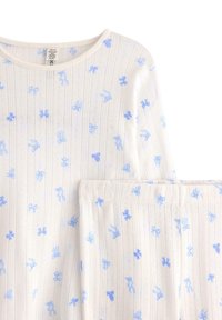 Ensemble de pyjama blanc en coton biologique recyclé, avec des motifs de nœuds bleu clair et une texture à côtes verticales sur le tissu.