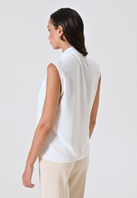 Weiße ärmellose Bluse mit einem Stehkragen, hergestellt aus einem glatten Stoff. Verfügt über einen geraden Schnitt und einen subtilen Glanz, präsentiert an einem Model von hinten.