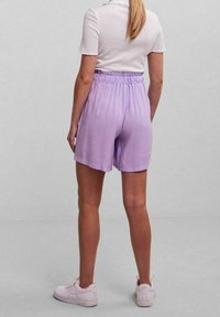 Lila, knälånga shorts med elastisk midja och slät textur. Matcher med en vit topp med kort ärm och vita sneakers.