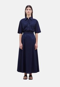 Vestido camisero azul marino con cuello, mangas cortas y cintura ceñida, que presenta una parte delantera con botones y un bolsillo. Tejido suave, de longitud hasta los tobillos.