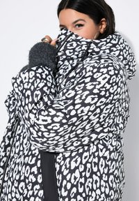 Chaqueta tipo puffer con estampado de leopardo en blanco y negro, cuenta con un cuello alto, cierre de cremallera y puños de punto gris texturizado.