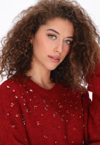 Czerwona sweter z dzianiny o fakturowanym wykończeniu, ozdobiony przezroczystymi i czerwonymi kamieniami rozsianymi po przodzie.