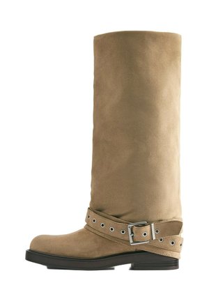 Botte haute jusqu'au genou en daim beige avec semelle noire et bride décorative avec boucle argentée autour de la cheville.