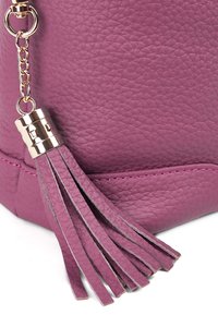 Lila Lederhandtasche mit strukturiertem Finish, ausgestattet mit einem Zubehör aus goldfarbenem Metall in Form eines Quastenakzents. Die Nähte sind in einer passenden Schattierung von Pink gehalten.