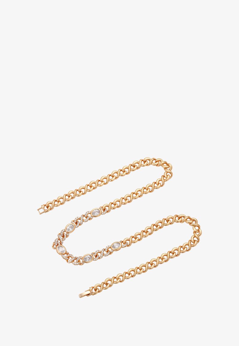 Guldkæde med ovale og runde klare ædelsten sat i dekorative led, anlagt i en løs zigzag på hvid baggrund.