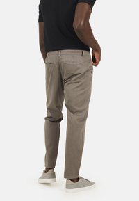 Chinos beige con vestibilità dritta e tasche laterali, realizzati in un morbido tessuto misto cotone e con dettagli discreti sulle tasche posteriori.