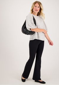 Blonde vrouw die een gestreepte lichtgrijze blouse draagt, zwarte uitlopende broek, zwarte platte schoenen, met een zwarte schoudertas met studs.