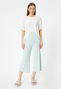 T-shirt blanc à manches courtes avec une poche, associé à un pantalon large à motif paisley bleu clair et des chaussons gris en peluche.