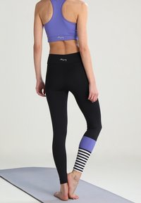 Czarne legginsy z fioletowym panelem i paskowanym akcentem na dolnej części nogi; zestawione z pasującym fioletowym stanik sportowym, z tyłem typu racerback.