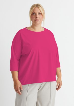 Fuchsia übergroßes Oberteil mit Rundhalsausschnitt und dreiviertel Ärmeln, featuring eine glatte Textur und eine lockere Passform, kombiniert mit hellen Hosen.